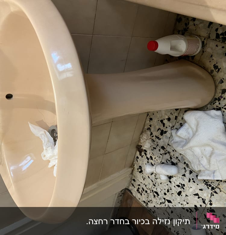 כיור עם ברז, בקבוק חומר ניקוי ומגבת על הרצפה